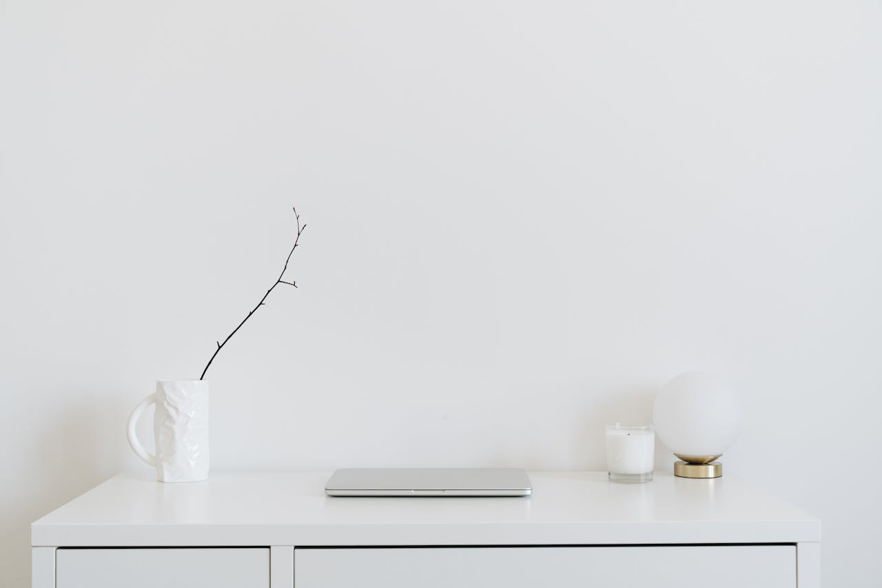 A clean, minimalistic workspace featuring a white desk, laptop, and decorative items, perfect for modern design inspiration.