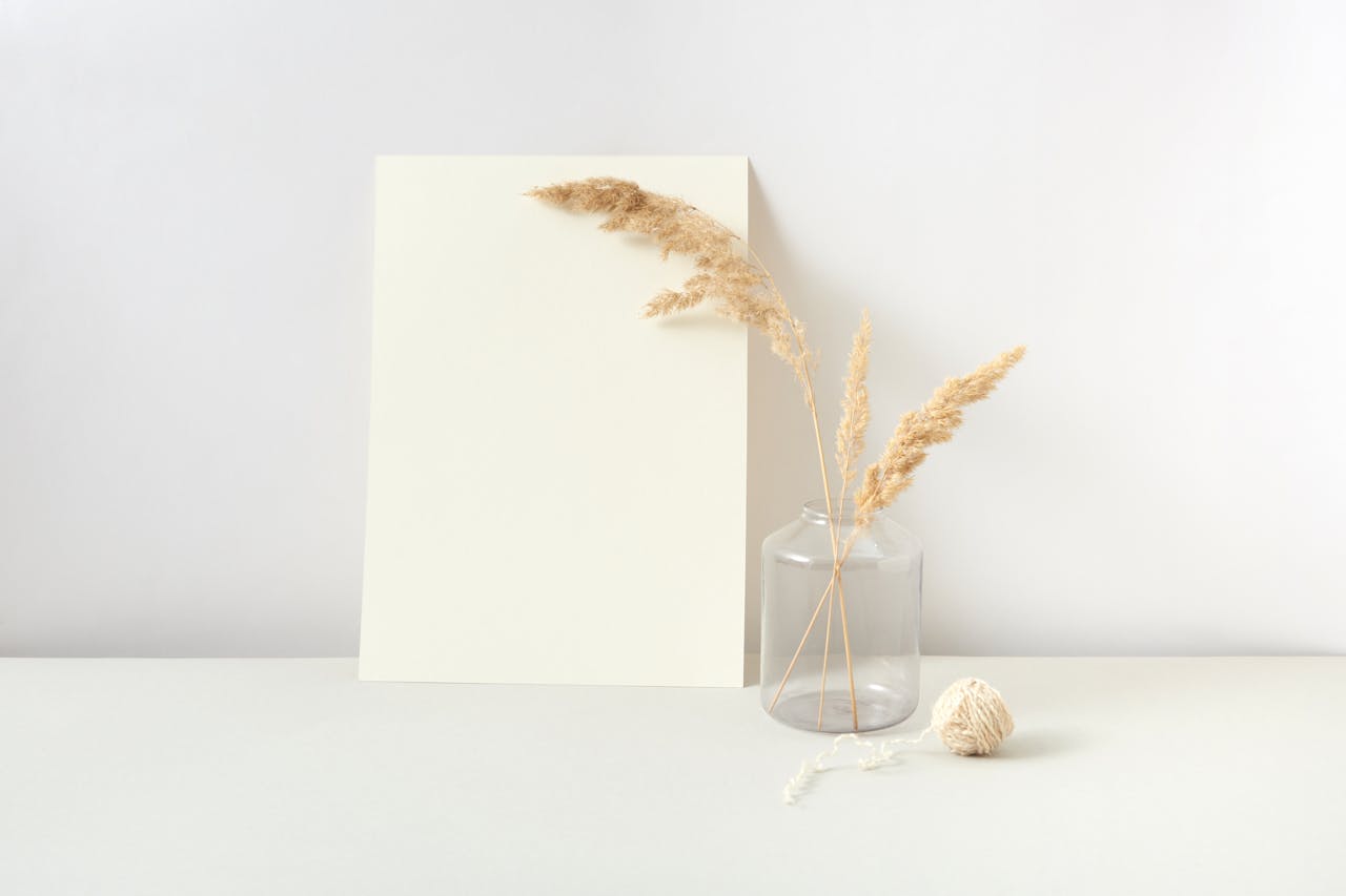 A minimalist composition featuring pampas grass in a glass jar, white paper, and yarn.