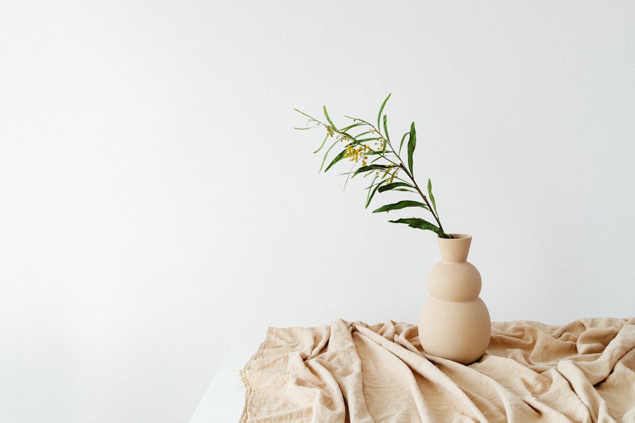Serene minimalist scene with a ceramic vase and greenery atop a beige textile, perfect for contemplative spaces.
